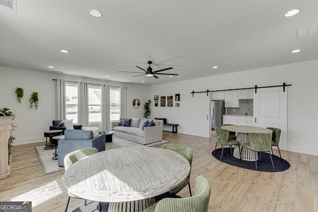 living room with ceiling fan, a barn door, sink, and light wood-type flooring