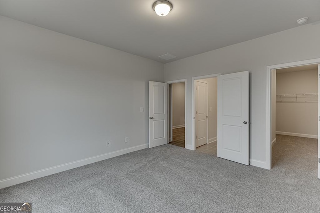 unfurnished bedroom with a closet, a spacious closet, and light carpet