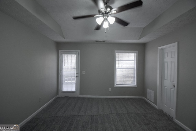 carpeted empty room with a textured ceiling, a tray ceiling, ceiling fan, and a healthy amount of sunlight