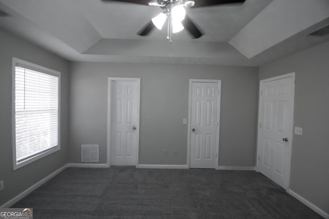 unfurnished bedroom featuring a tray ceiling, ceiling fan, and dark colored carpet