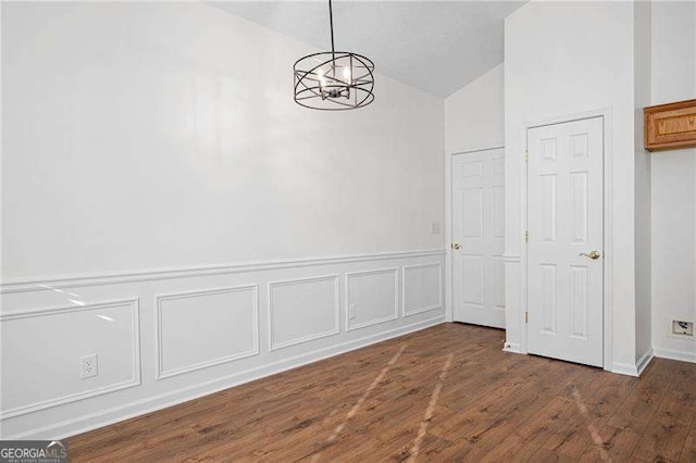 unfurnished dining area with dark hardwood / wood-style flooring, lofted ceiling, and a chandelier