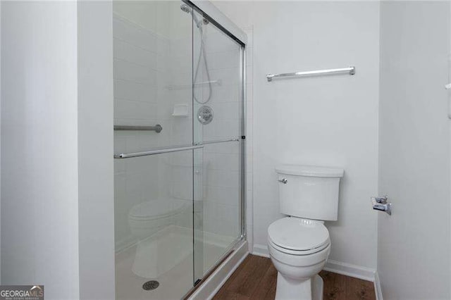 bathroom with hardwood / wood-style flooring, a shower with shower door, and toilet