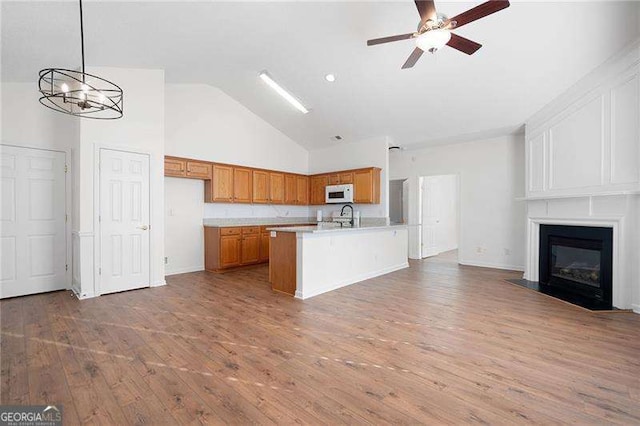 kitchen featuring sink, hanging light fixtures, a large fireplace, a center island with sink, and light wood-type flooring