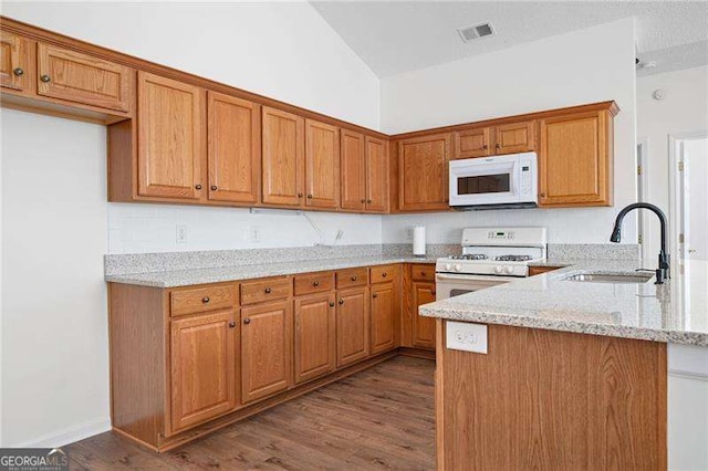 kitchen with vaulted ceiling, sink, light stone counters, kitchen peninsula, and white appliances