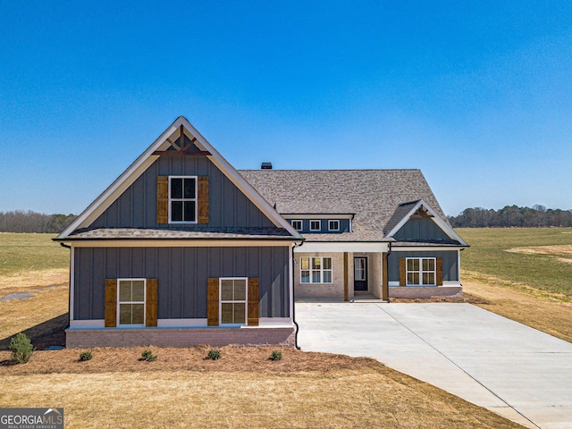 view of front of home with board and batten siding, concrete driveway, a front lawn, and roof with shingles