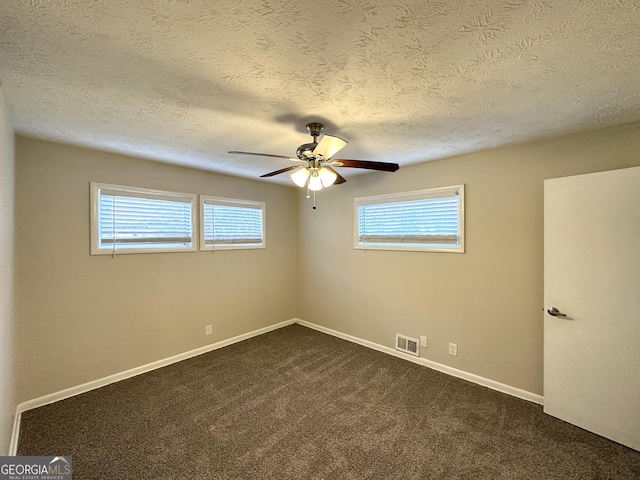 spare room featuring a wealth of natural light, ceiling fan, dark carpet, and a textured ceiling