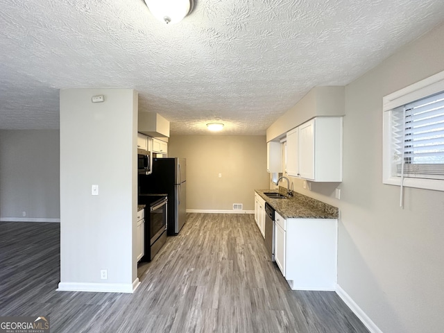 kitchen featuring appliances with stainless steel finishes, dark stone counters, sink, hardwood / wood-style flooring, and white cabinets