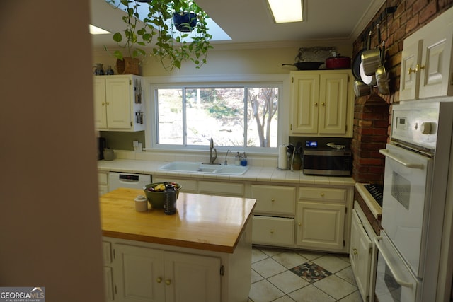 kitchen featuring tile countertops, sink, light tile patterned floors, white dishwasher, and crown molding