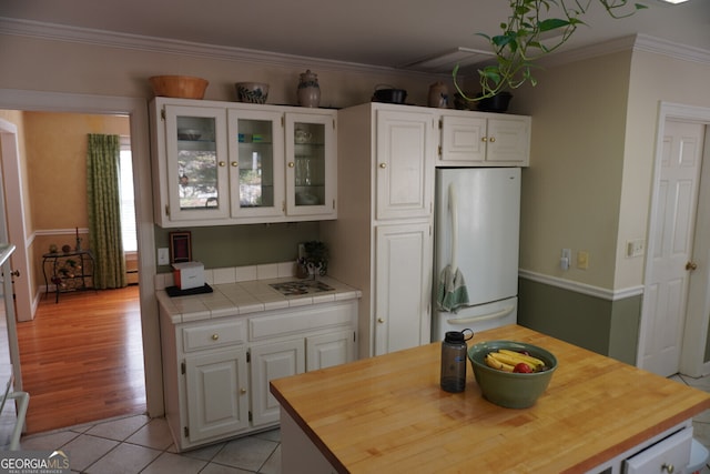 kitchen featuring crown molding, tile countertops, light tile patterned floors, white fridge, and white cabinets