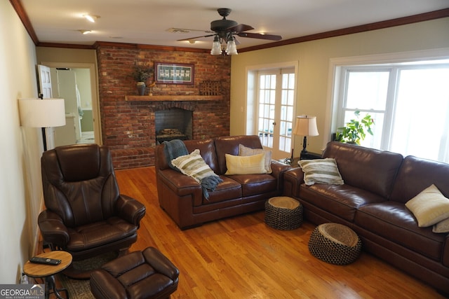 living room with light hardwood / wood-style flooring, ceiling fan, ornamental molding, a brick fireplace, and french doors