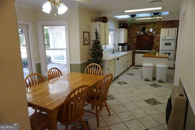 tiled dining space with sink, crown molding, a skylight, ceiling fan, and brick wall