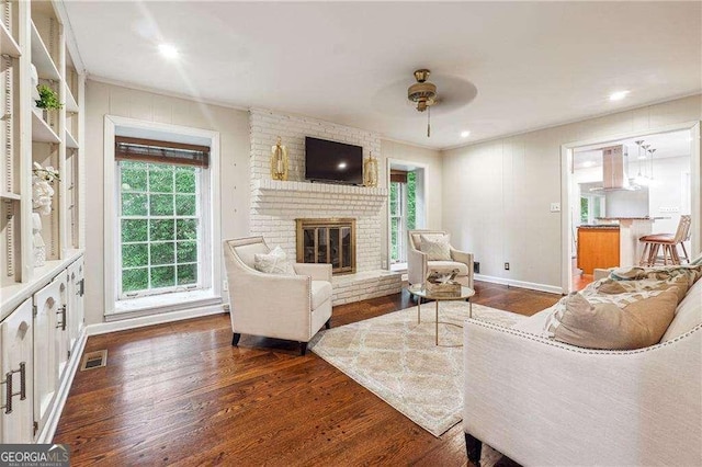 living room featuring ceiling fan, dark hardwood / wood-style flooring, and a brick fireplace