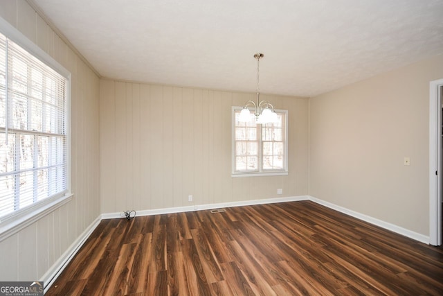 spare room with dark wood-type flooring and an inviting chandelier