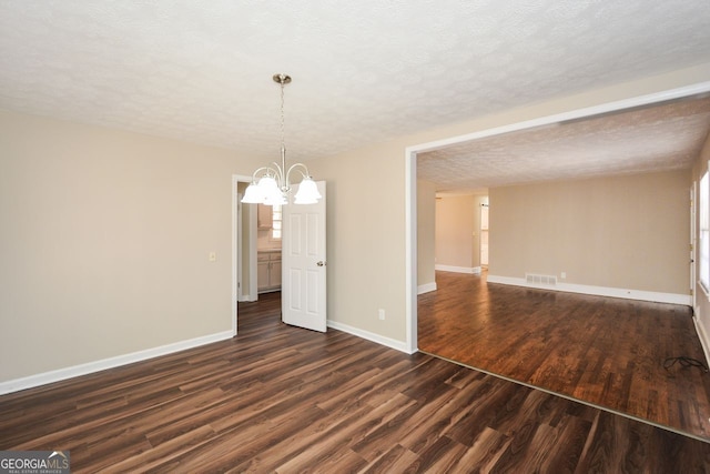 unfurnished room featuring dark hardwood / wood-style floors, a chandelier, and a textured ceiling