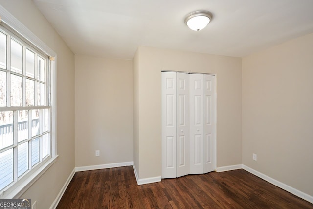 unfurnished bedroom with a closet, dark hardwood / wood-style floors, and multiple windows