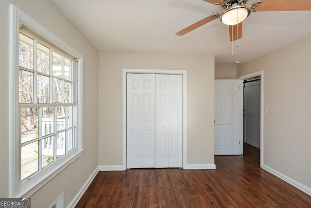 unfurnished bedroom with ceiling fan, multiple windows, dark hardwood / wood-style floors, and a closet