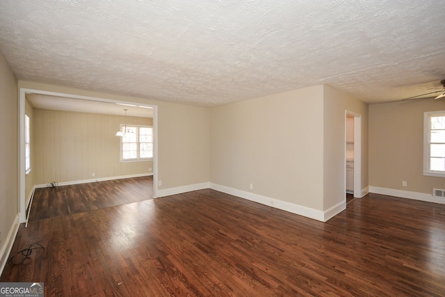 empty room with dark wood-type flooring, ceiling fan with notable chandelier, and a textured ceiling