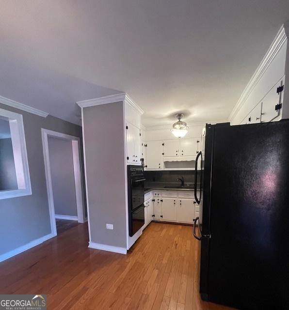 kitchen featuring sink, crown molding, white cabinets, black appliances, and light wood-type flooring