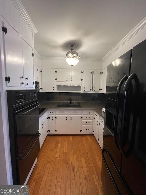 kitchen with white cabinetry, ornamental molding, black appliances, and light wood-type flooring