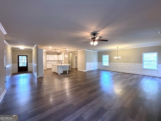 unfurnished living room featuring ceiling fan with notable chandelier, crown molding, plenty of natural light, and dark wood-type flooring