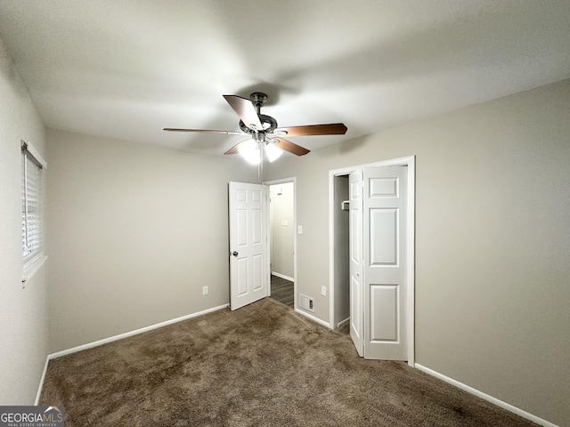 unfurnished bedroom with dark colored carpet, a closet, and ceiling fan