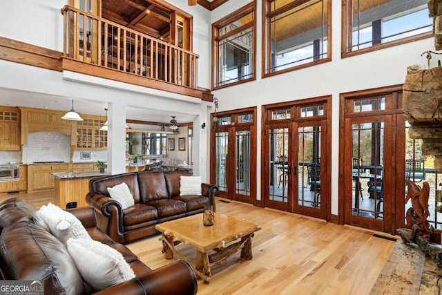 living room with ceiling fan, french doors, a high ceiling, light wood-type flooring, and ornamental molding