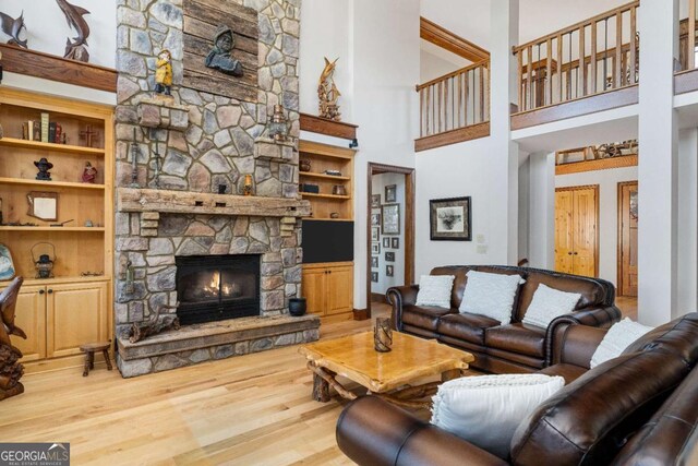 living room featuring a fireplace, built in features, a towering ceiling, and hardwood / wood-style floors