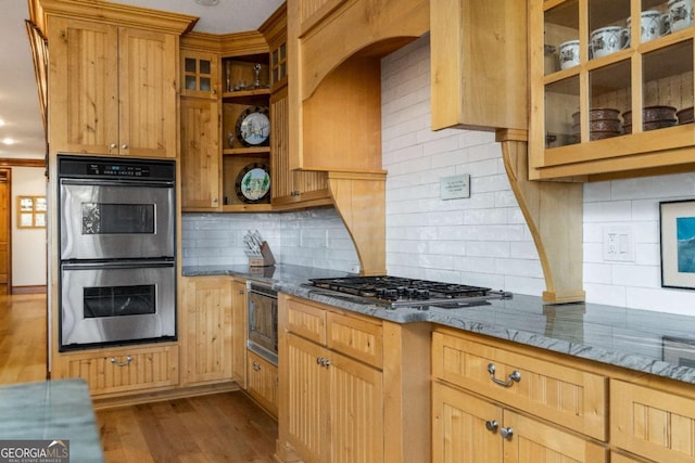 kitchen featuring backsplash, dark stone countertops, stainless steel appliances, and light hardwood / wood-style flooring