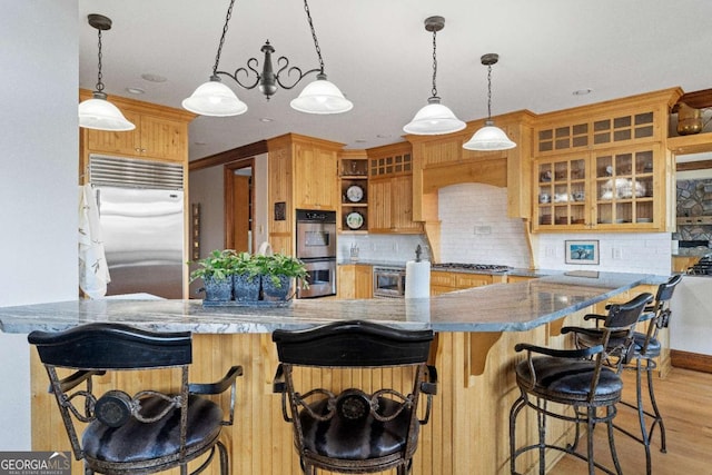 kitchen featuring pendant lighting, built in appliances, light wood-type flooring, kitchen peninsula, and a breakfast bar area