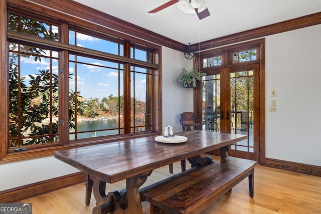 dining area with french doors, a water view, light wood-type flooring, and ornamental molding