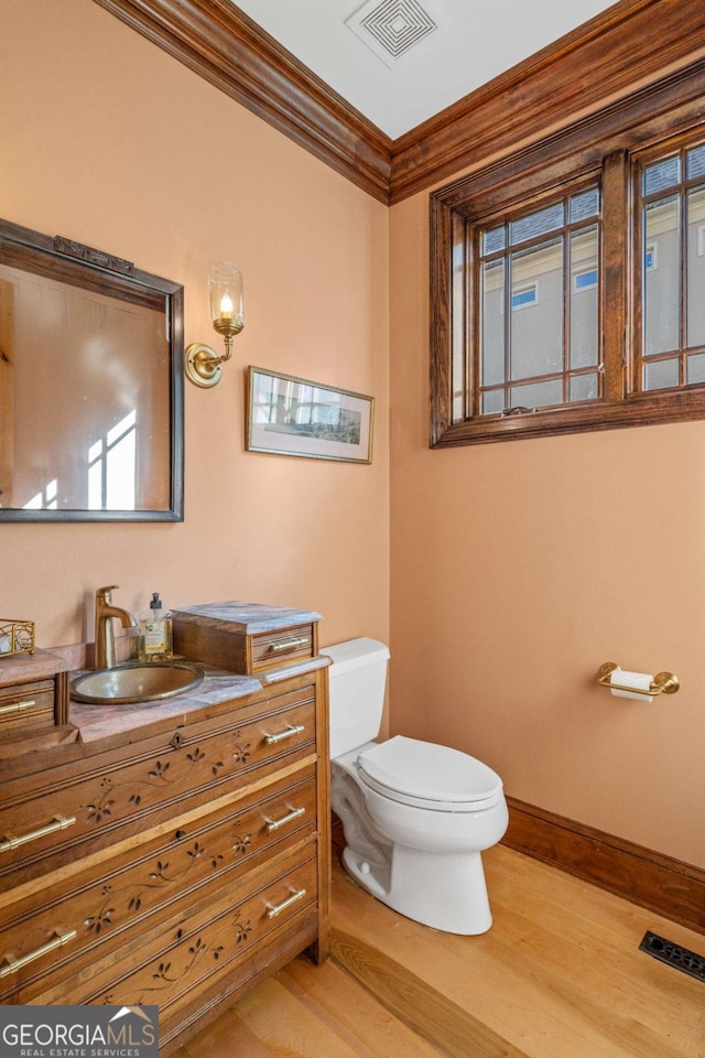 bathroom featuring wood-type flooring, vanity, toilet, and crown molding