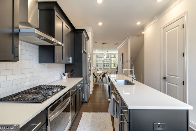 kitchen featuring dark wood-type flooring, wall chimney range hood, sink, an island with sink, and stainless steel appliances