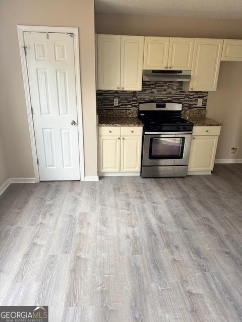 kitchen with decorative backsplash, stainless steel range oven, dark stone counters, and light hardwood / wood-style flooring