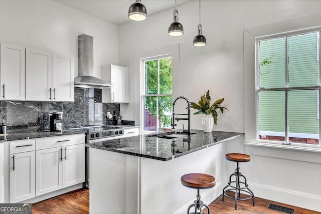 kitchen with sink, wall chimney range hood, dark hardwood / wood-style floors, dark stone countertops, and white cabinets