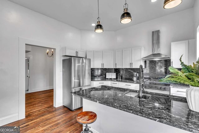 kitchen with dark stone counters, wall chimney exhaust hood, stainless steel fridge, decorative backsplash, and dark hardwood / wood-style flooring