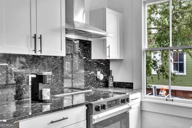 kitchen featuring backsplash, high end stainless steel range oven, wall chimney range hood, dark stone countertops, and white cabinetry