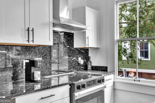 kitchen featuring wall chimney exhaust hood, dark stone countertops, white cabinetry, and stainless steel range