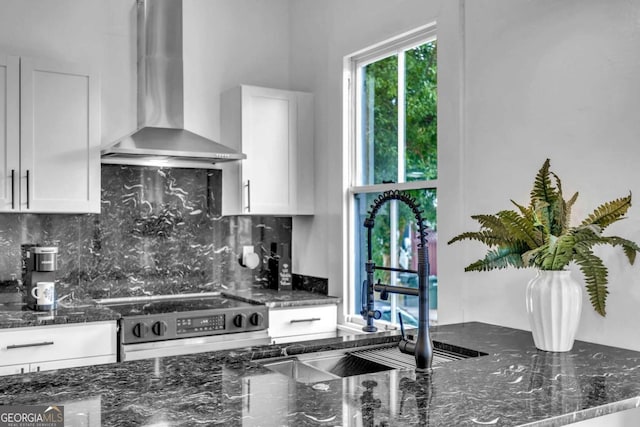 kitchen featuring tasteful backsplash, white cabinetry, wall chimney exhaust hood, and range