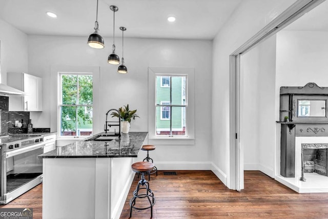 kitchen with white cabinetry, dark hardwood / wood-style flooring, dark stone countertops, pendant lighting, and stainless steel stove