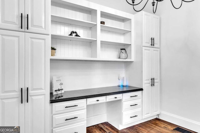 bar with white cabinets, dark hardwood / wood-style floors, built in desk, and a notable chandelier