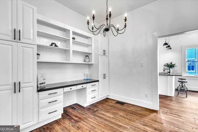 kitchen with white cabinetry, built in desk, decorative light fixtures, and dark hardwood / wood-style floors