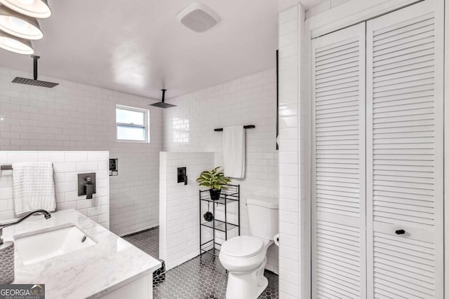 bathroom featuring vanity, tile patterned flooring, toilet, tiled shower, and tile walls