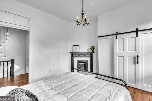 bedroom featuring a barn door, wood-type flooring, and an inviting chandelier