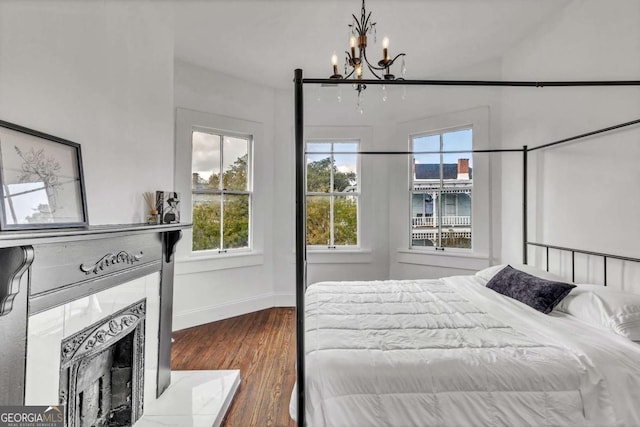 bedroom with a tile fireplace, dark hardwood / wood-style floors, an inviting chandelier, and multiple windows