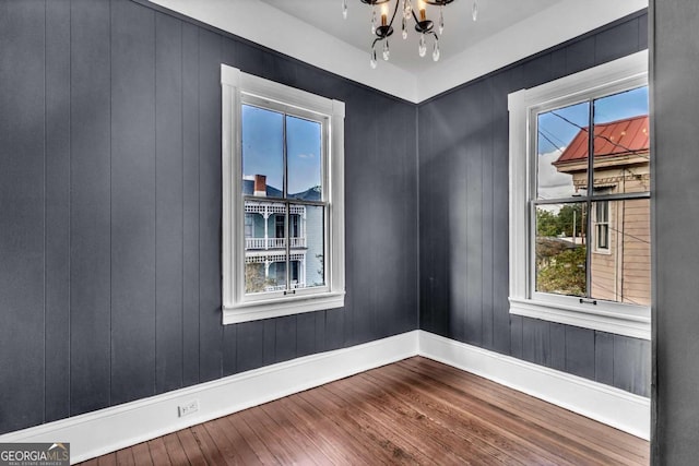 empty room with wooden walls, hardwood / wood-style floors, and a notable chandelier