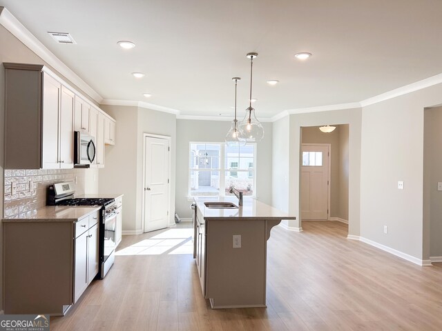 kitchen featuring appliances with stainless steel finishes, sink, light hardwood / wood-style flooring, hanging light fixtures, and an island with sink