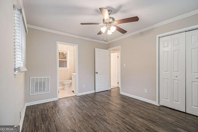 unfurnished bedroom featuring ensuite bath, ceiling fan, dark wood-type flooring, crown molding, and a closet