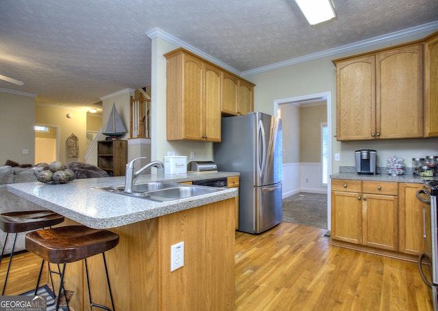 kitchen featuring sink, light hardwood / wood-style floors, a textured ceiling, a breakfast bar area, and ornamental molding