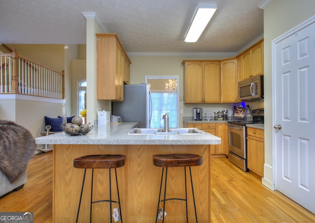 kitchen with light hardwood / wood-style flooring, ornamental molding, appliances with stainless steel finishes, a kitchen bar, and kitchen peninsula