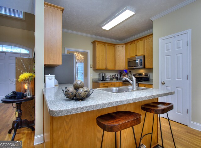 kitchen with sink, a kitchen breakfast bar, kitchen peninsula, crown molding, and light wood-type flooring